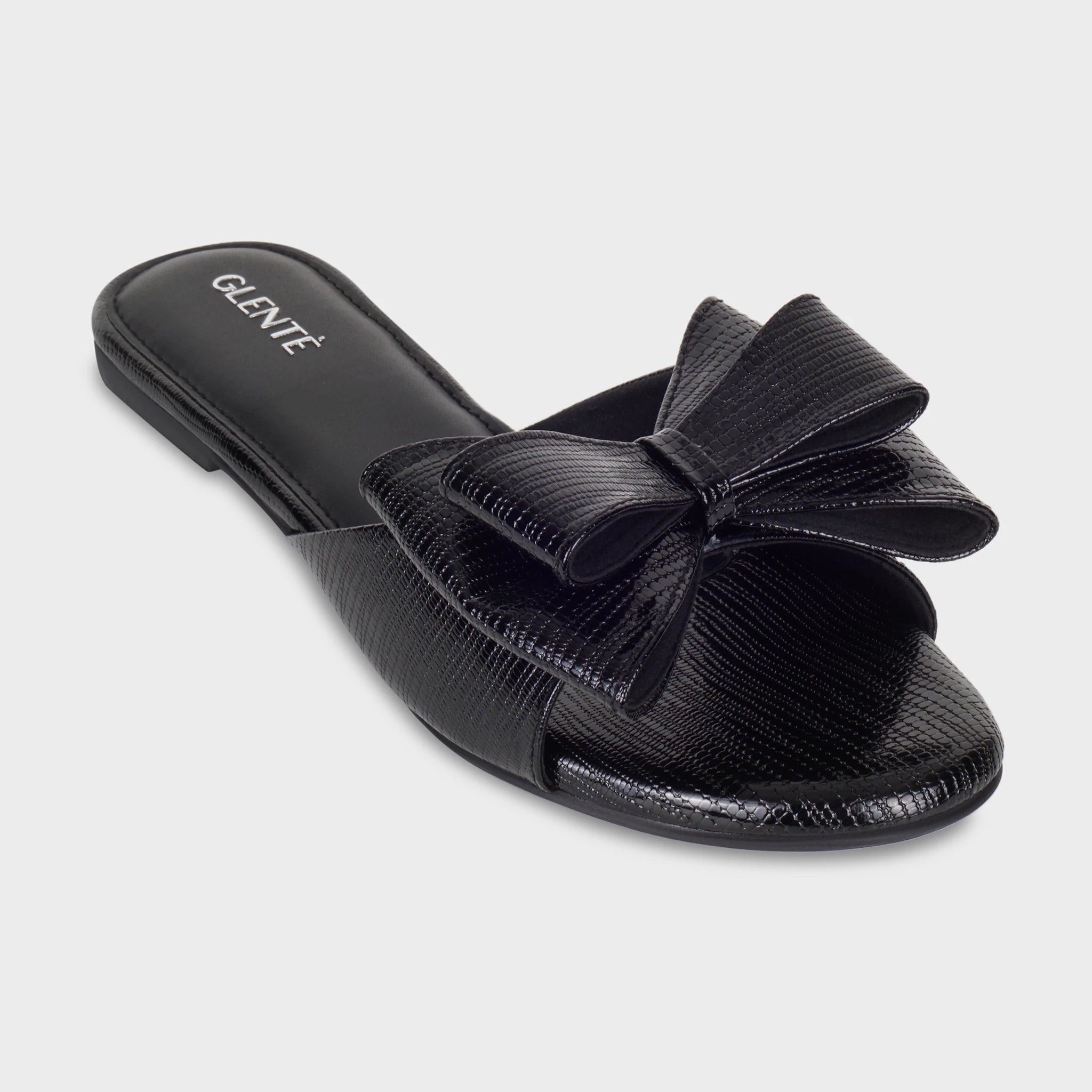 Front angled view of Alveria black lizard-embossed flat slides highlighting the structured double bow, wide strap construction, and silver Glentè branding on the black sole