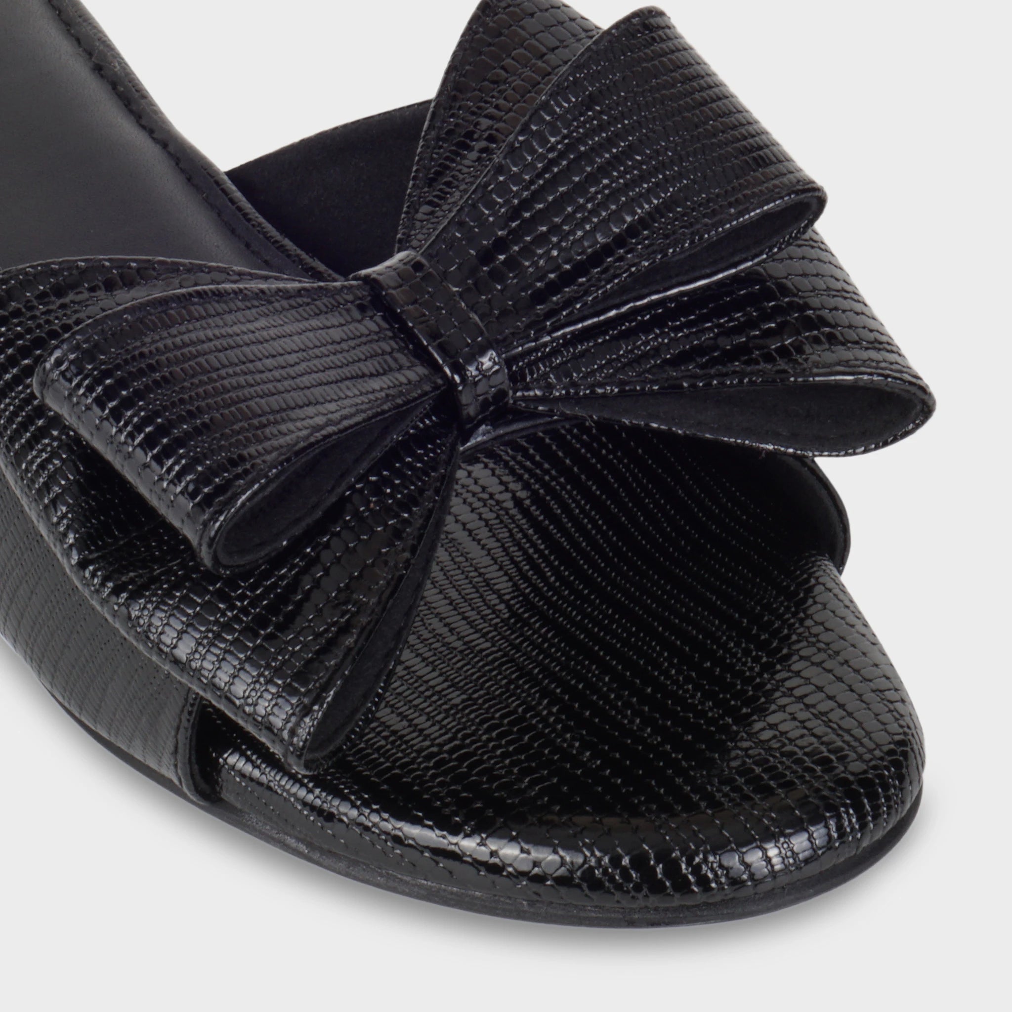 Close-up of the Alveria structured double bow detail showing the glossy lizard-emboss texture, precise center knot, and high-shine black finish - Glentè