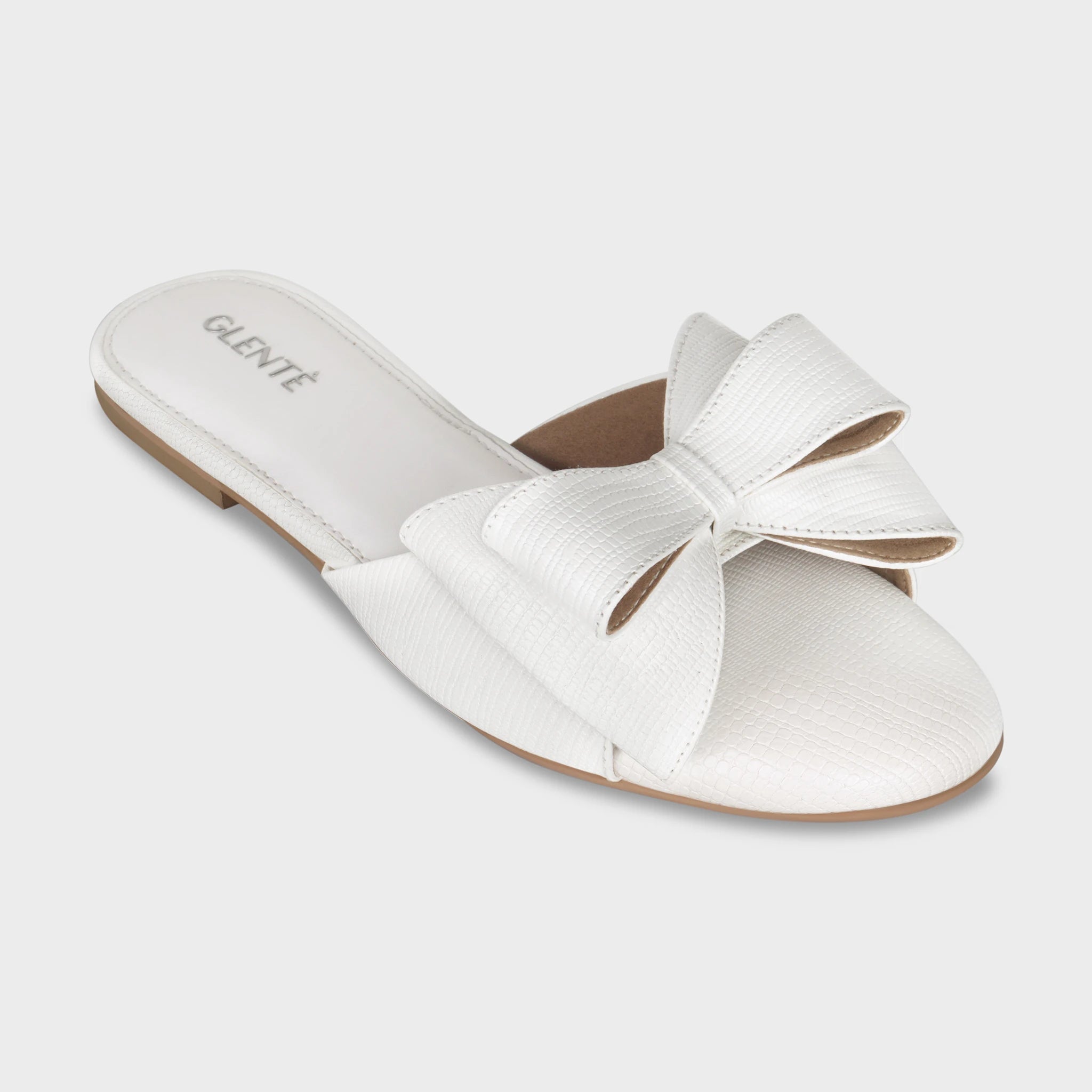 Front angled view of Alveria white lizard-embossed flat slides highlighting the statement double bow, open toe footbed, and silver Glentè logo on the white insole