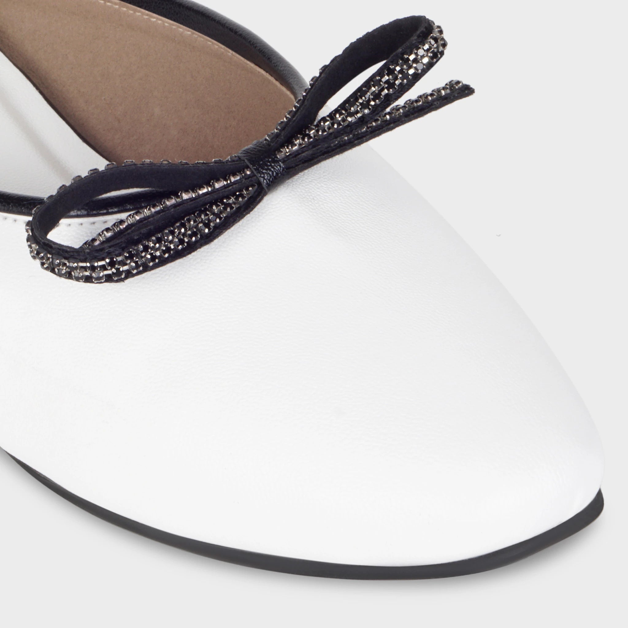 Close-up of the Auralin black crystal-encrusted bow detail showing individual rhinestone setting along each loop, contrast against the smooth white upper, and black piping trim - Glentè