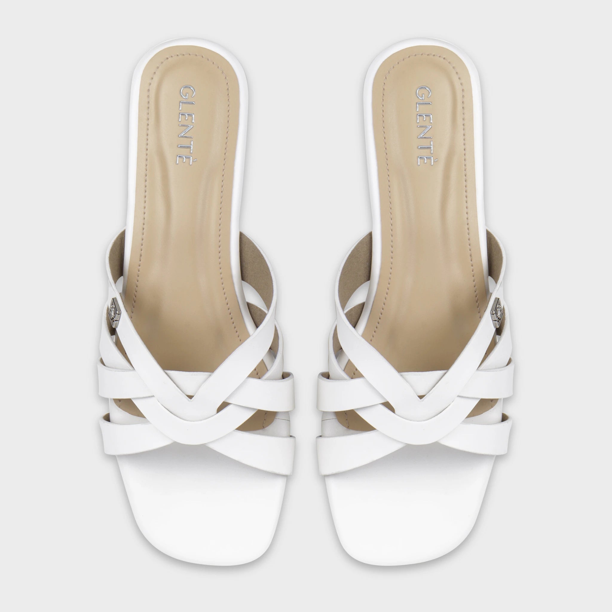 Top-down view of Averis white flat slides as a pair, showing the symmetrical woven multi-strap design, silver Glentè brand buckles, and silver branding on beige insoles