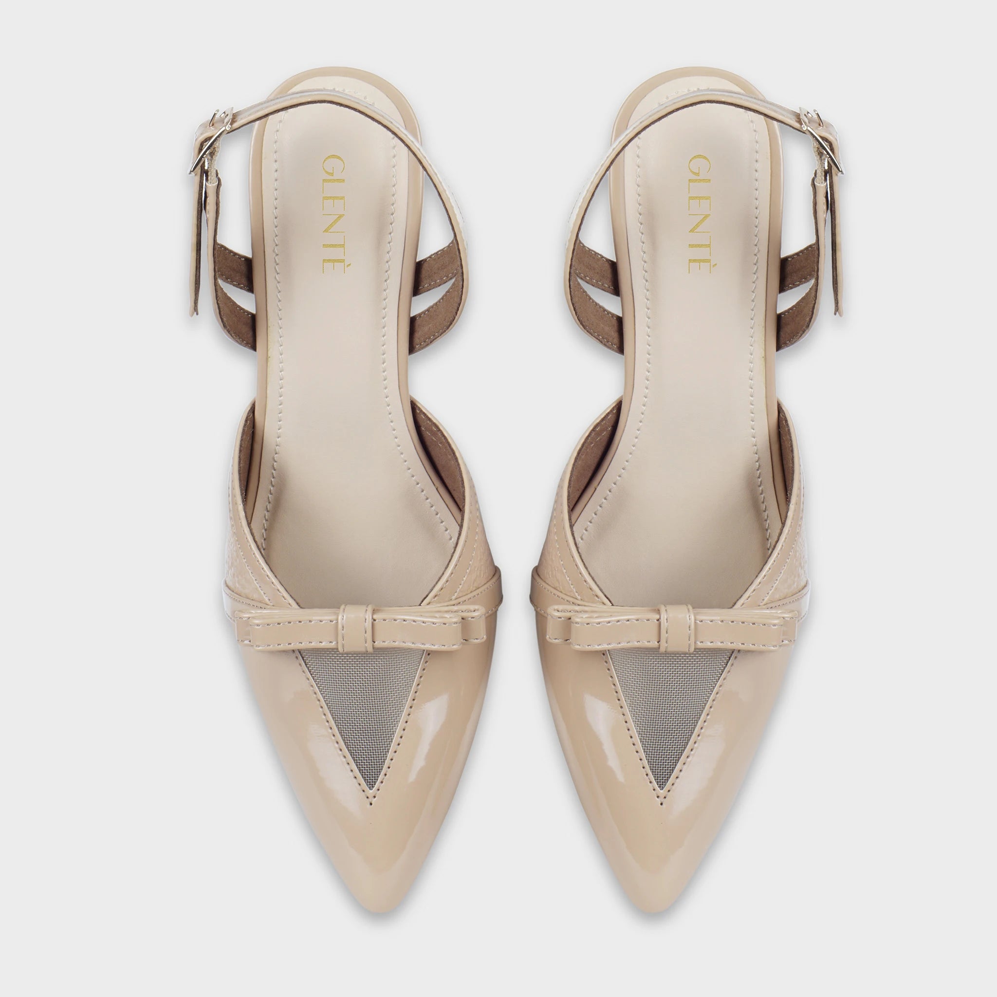 Top-down view of Celestrine nude patent slingback heels as a pair, showing the matching pointed toes, sheer mesh V-windows, tonal bow accents, and gold Glentè branding on nude insoles
