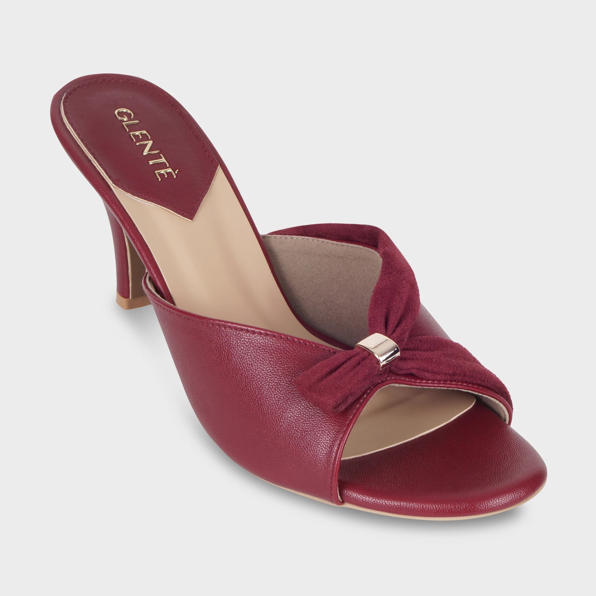 Front angled view of Solviane cherry red heeled mules highlighting the gathered suede knot with gold metal clasp, open toe, and gold Glentè branding on the insole