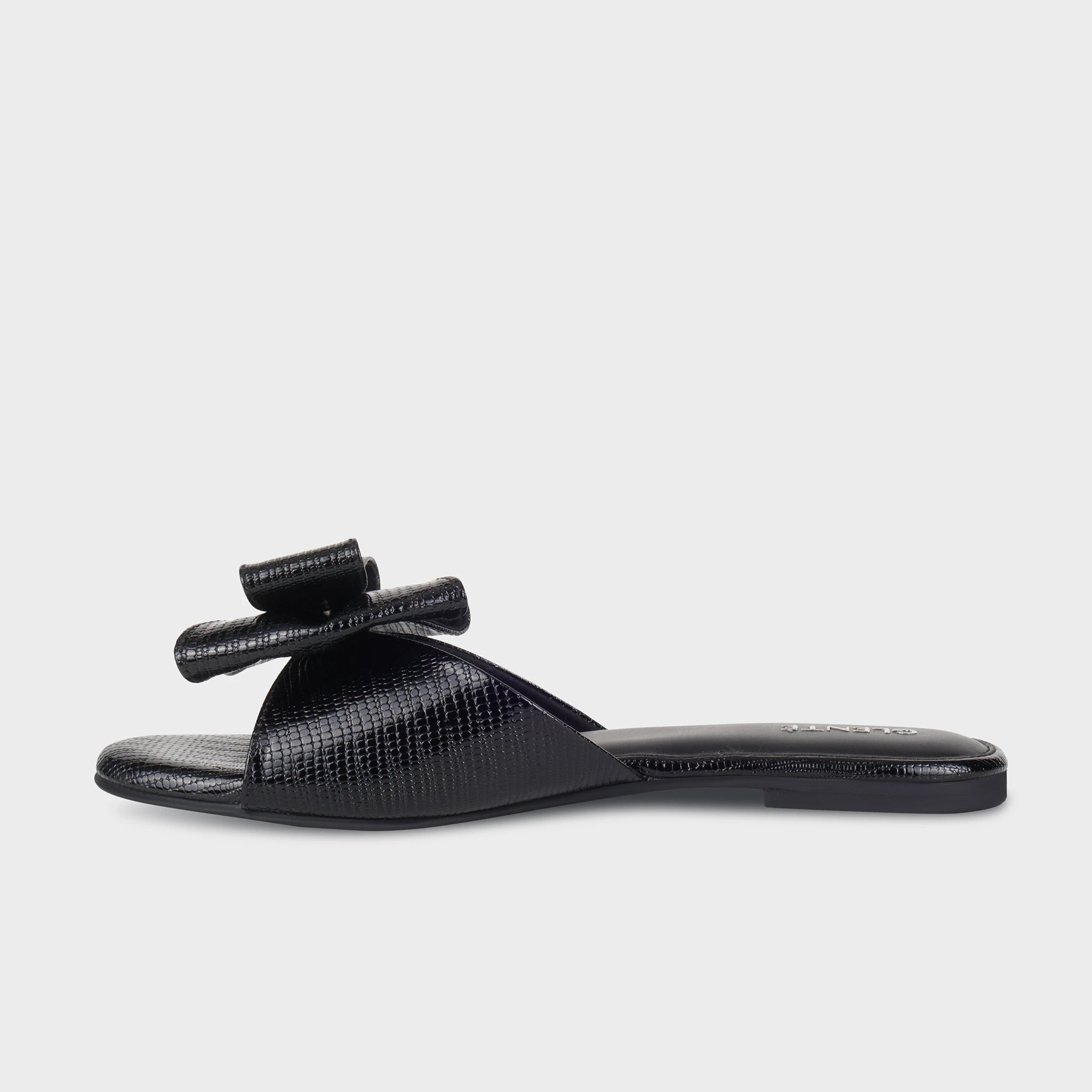 Inner side view of black Alveria flat slides showing the glossy lizard-emboss texture, layered bow detail, and slim black outsole - Glentè