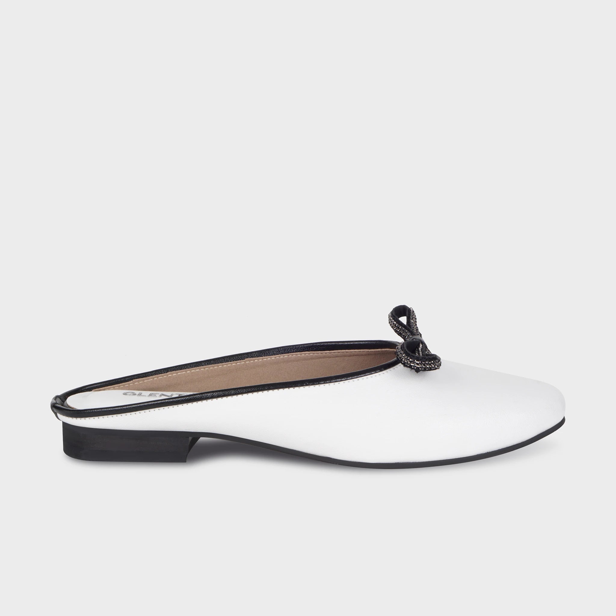 White closed-toe flat mules with black piping trim, a black crystal-embellished bow accent, and a low block heel - Glentè Auralin