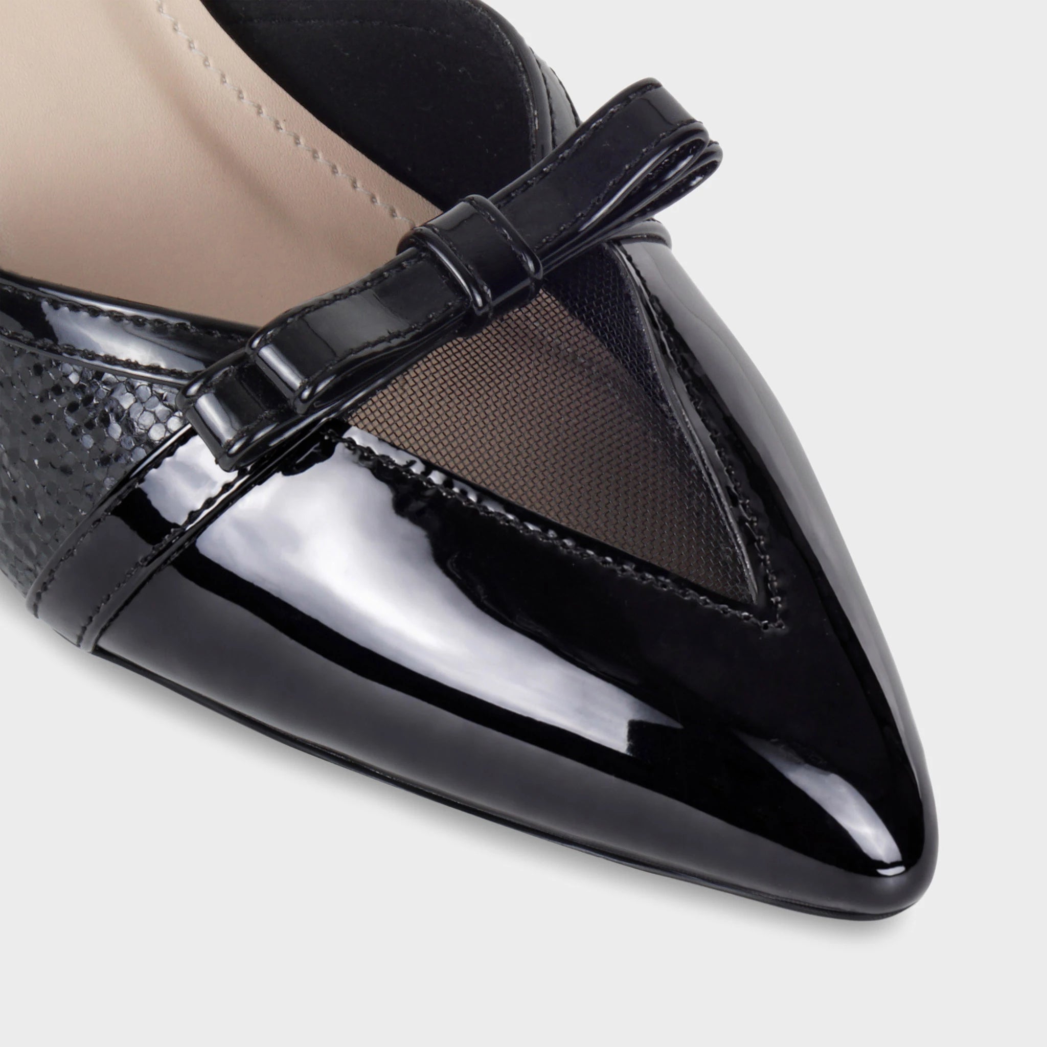 Close-up of the Celestrine pointed toe showing the mirror-finish black patent cap, sheer mesh triangular cutout, miniature patent bow, and where the snake-embossed panel meets the glossy upper - Glentè