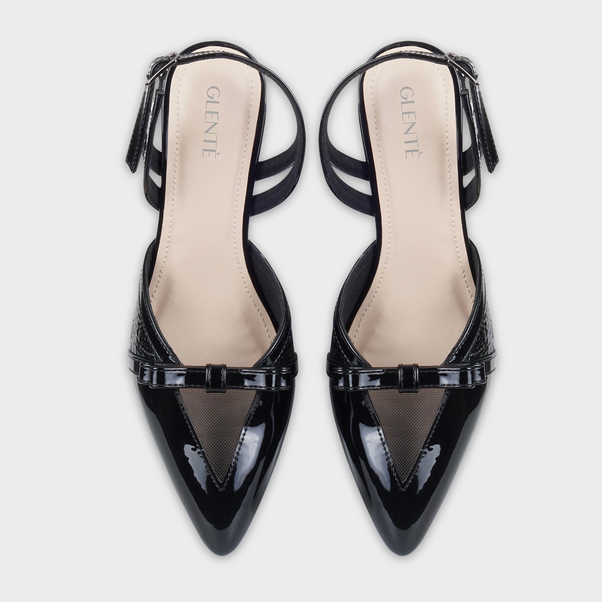Top-down view of Celestrine black patent slingback heels as a pair, showing the symmetrical pointed toes, sheer mesh V-inserts, patent bow accents, and Glentè branding on cream insoles