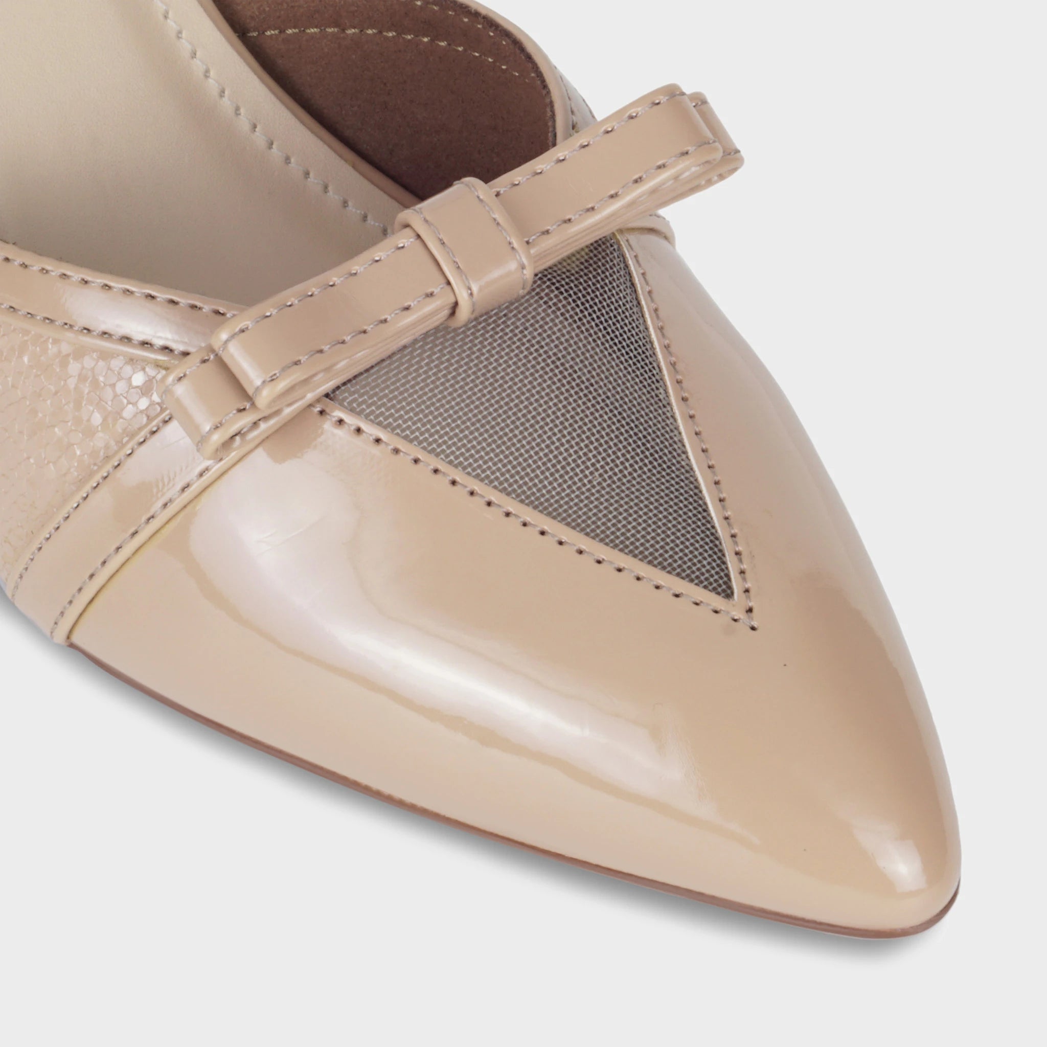 Close-up of the Celestrine pointed toe showing the warm nude patent finish, sheer mesh triangular detail framed by tonal stitching, and delicate patent bow sitting across the vamp - Glentè